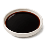 Dark soy sauce in a low warm off-white ceramic condiment dish, with a near-black mahogany-brown center and a narrow deep reddish-brown translucent edge.