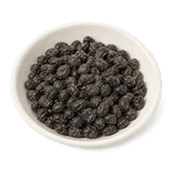 Wrinkled black-brown fermented black beans in a plain ivory ceramic dish on a pure white background.