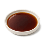 Reddish-brown light soy sauce in a low warm off-white ceramic condiment dish on a pure white background.