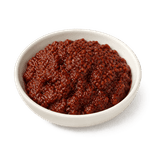 Deep red-brown Pixian doubanjiang in a plain ivory ceramic condiment dish on a pure white background.