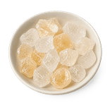 Irregular clear-to-pale-amber rock sugar crystals in a low matte warm-white dish on a pure white background.